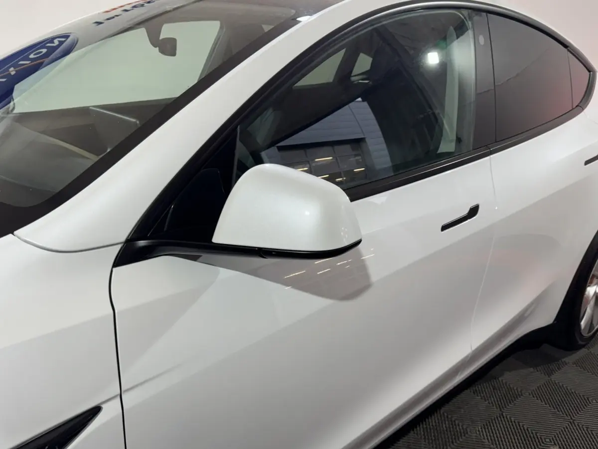 Vue de profil côté gauche d'une Tesla Model Y blanche avec rétroviseur et poignées de porte intégrées.