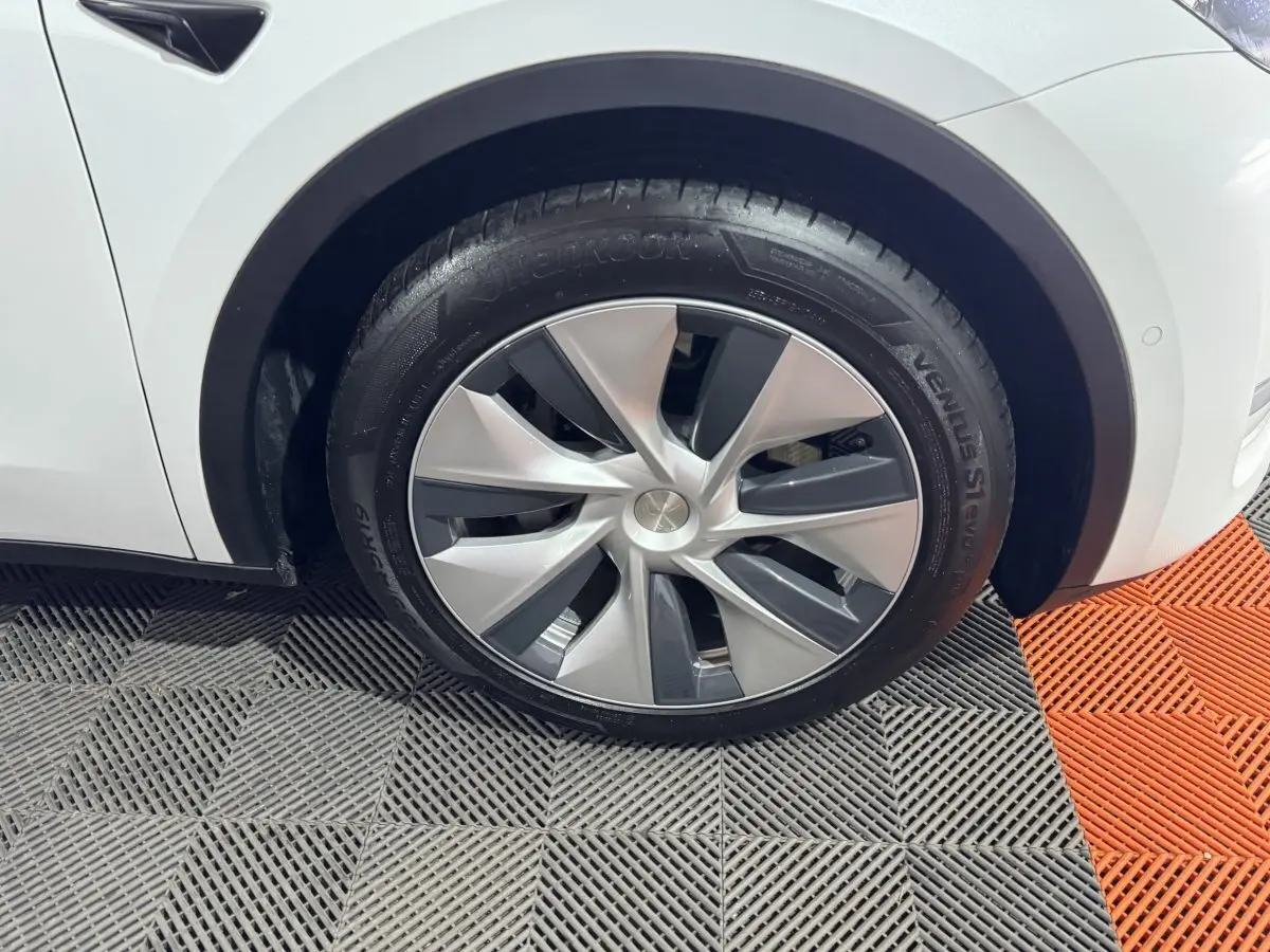 Gros plan sur la roue avant gauche d'une Tesla Model Y blanche, avec jante aérodynamique et pneu Hankook.