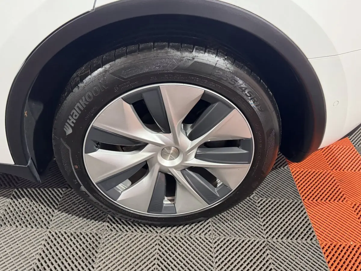 Gros plan sur la roue avant droite d'une Tesla Model Y blanche, jante aérodynamique grise et noire.