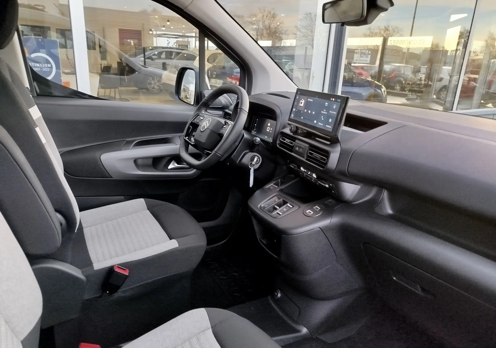 Vue intérieure côté conducteur du Citroën Berlingo 2025 avec sièges gris, tableau de bord noir et écran tactile central.
