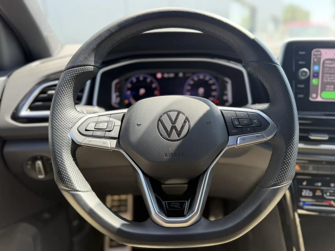 Vue rapprochée du volant sport en cuir noir avec logo R-Line du Volkswagen T-Roc 2025, tableau de bord digital en arrière-plan.