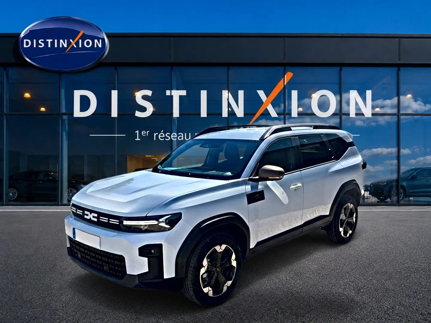 SUV Dacia Bigster blanc vu en 3/4 avant droit, avec barres de toit et jantes alu distinctives.