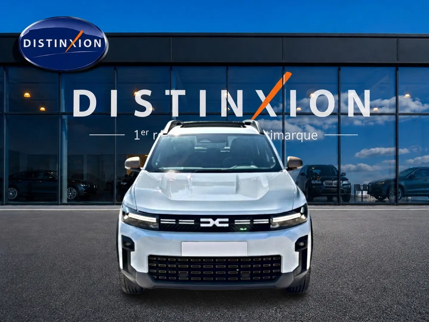 Vue frontale du Dacia Bigster blanc avec calandre noire et logo distinctif, devant une vitrine Distinxion.