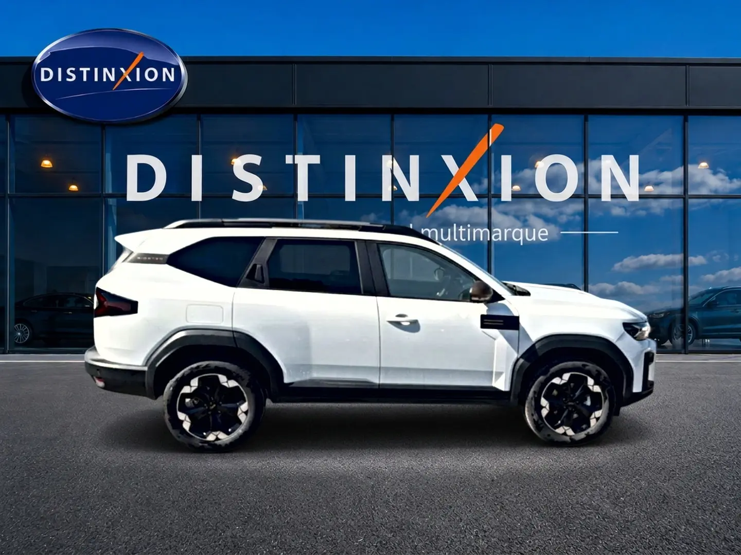 Profil droit du Dacia Bigster blanc 2026 avec jantes noires et toit contrasté devant une vitrine Distinxion.