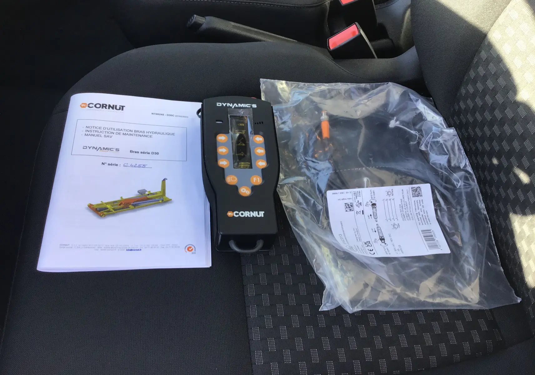 Vue intérieure sur siège avant droit montrant notice, télécommande et câble du bras de levage Cornut dans un Ford Transit blanc.