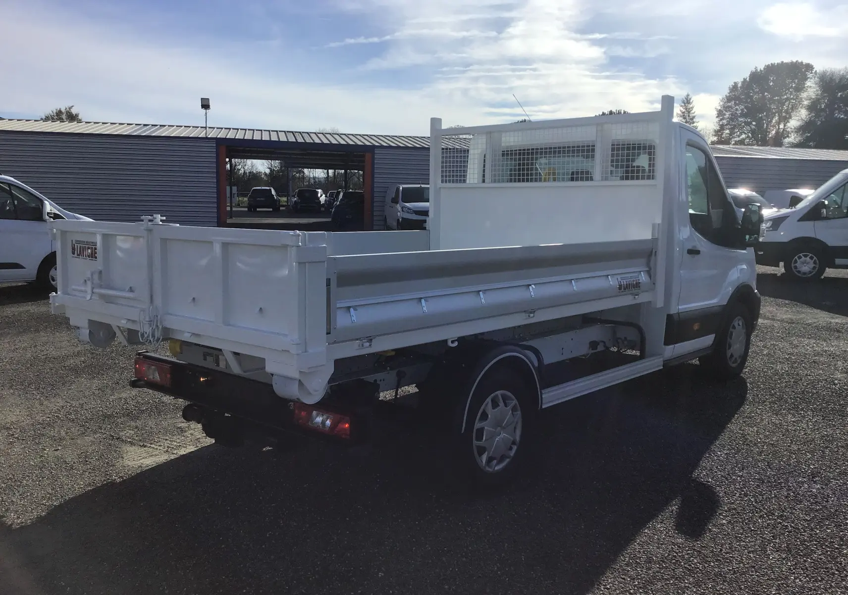 Vue 3/4 arrière droit d'un Ford Transit Chassis Cabine blanc avec benne et portes battantes, stationné en extérieur.