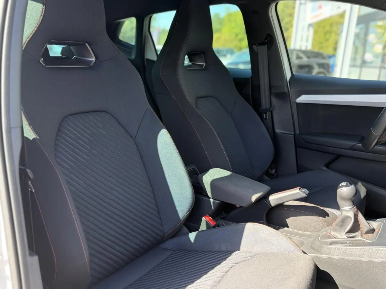 Vue intérieure côté conducteur de la SEAT Ibiza TSI 115 FR 2025, sièges sport noirs avec surpiqûres rouges et levier de vitesse manuel.