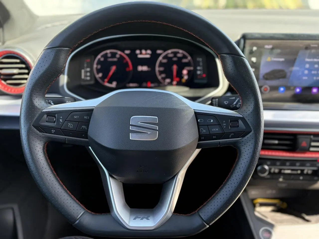 Vue rapprochée du volant perforé noir avec surpiqûres rouges et tableau de bord digital de la SEAT Ibiza TSI 115 FR 2025.