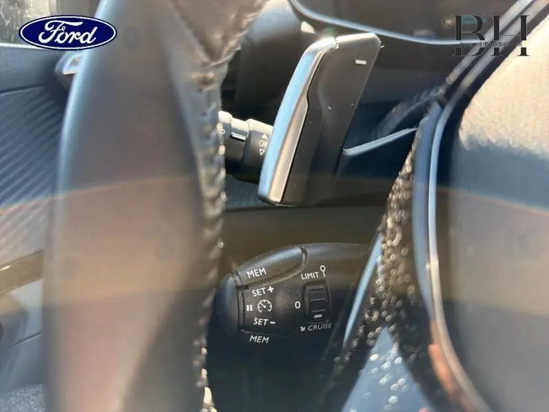 Gros plan sur la commande de régulateur de vitesse derrière le volant d’un Peugeot 2008 blanc nacré.