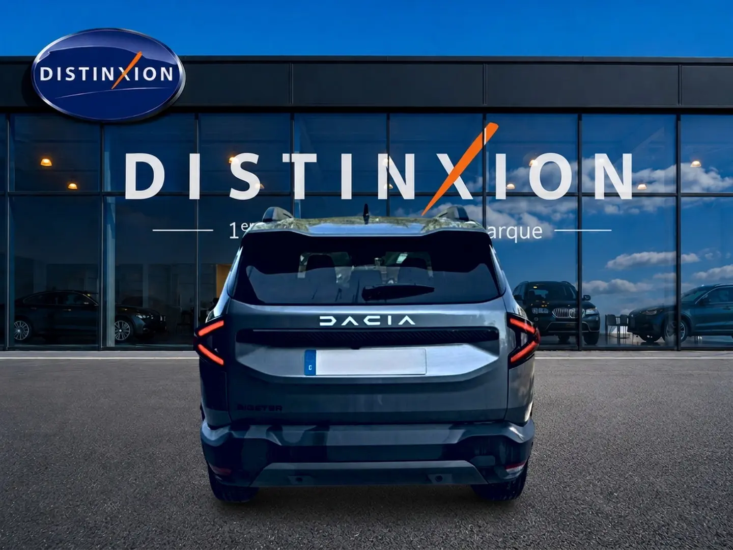 Vue arrière d'un Dacia Bigster gris schiste, avec feux arrière LED en forme de flèche, devant une vitrine Distinxion.