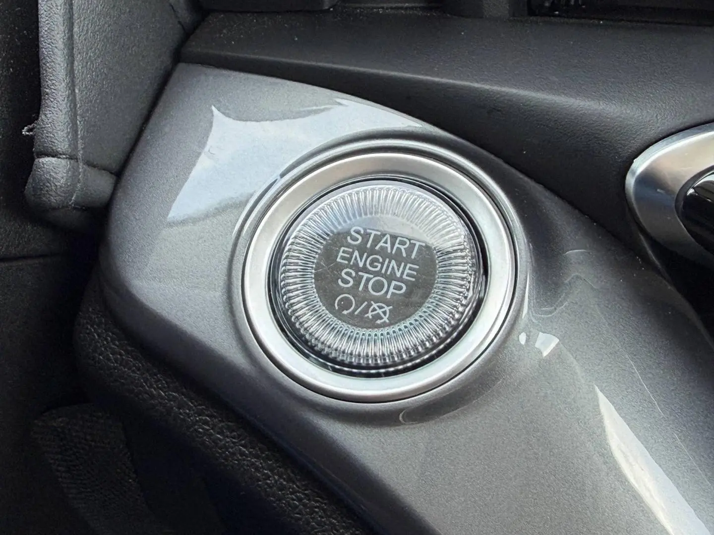Gros plan sur le bouton Start Engine Stop gris brillant du tableau de bord de la Fiat 500 électrique blanche 2023.