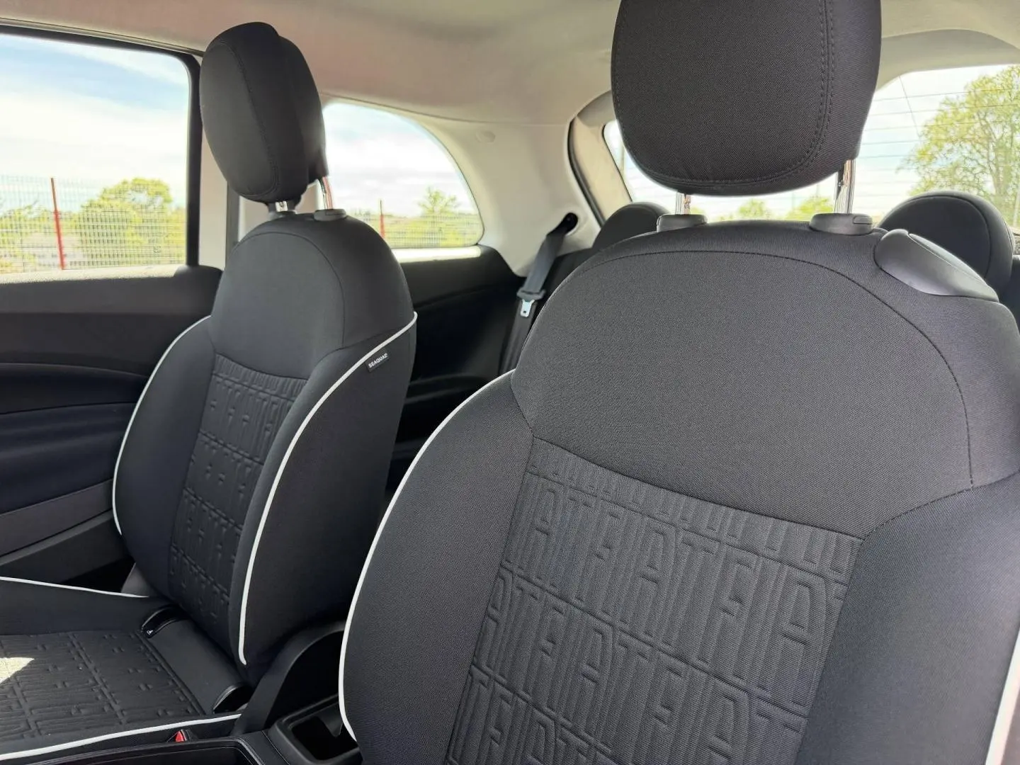 Gros plan sur les sièges avant noirs de la Fiat 500 e 118ch MY23 avec motif monogramme Fiat et surpiqûres blanches.