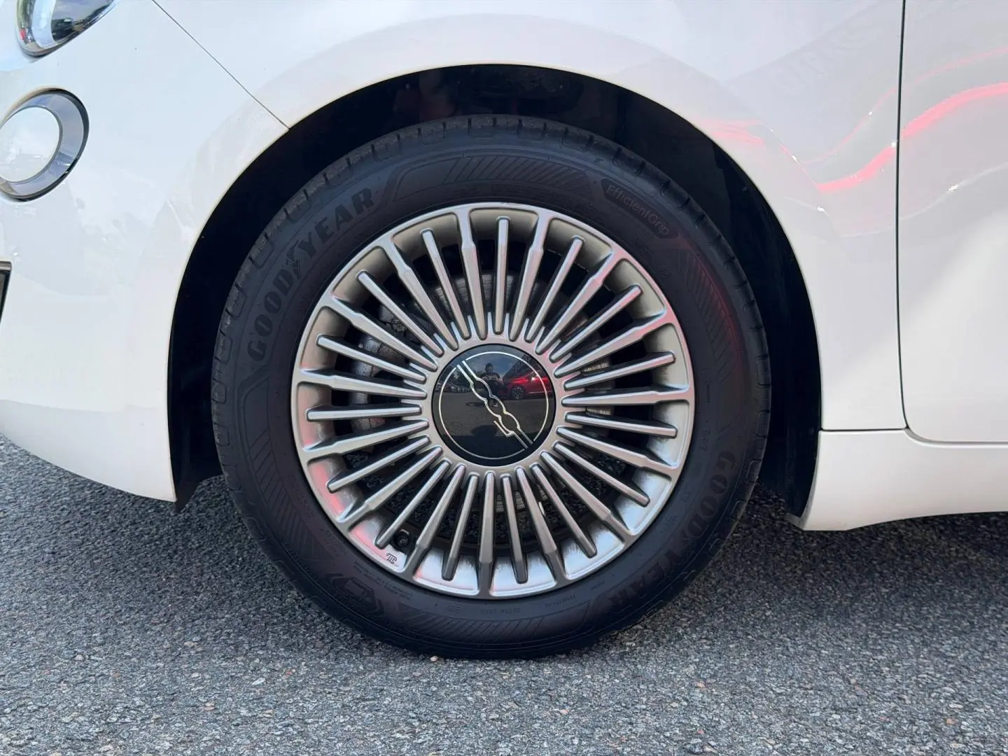 Gros plan sur la roue avant droite d'une Fiat 500 e blanche, avec jante argentée au design rayonné distinctif.