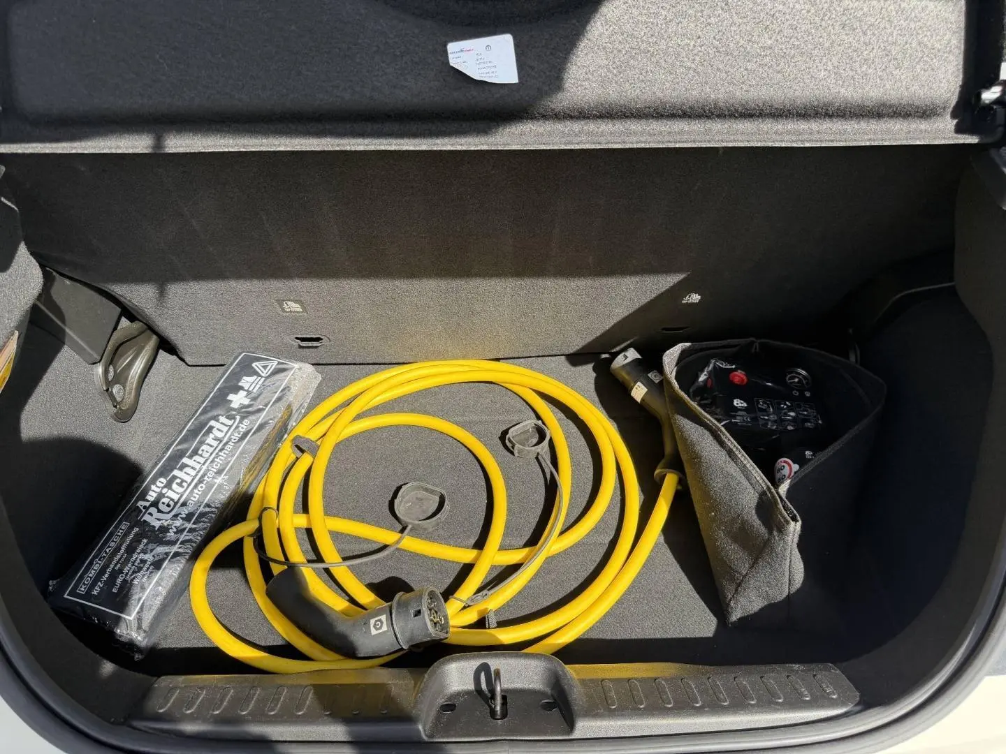 Coffre ouvert de la Fiat 500 électrique blanche MY23 montrant un câble de recharge jaune et un kit de secours.