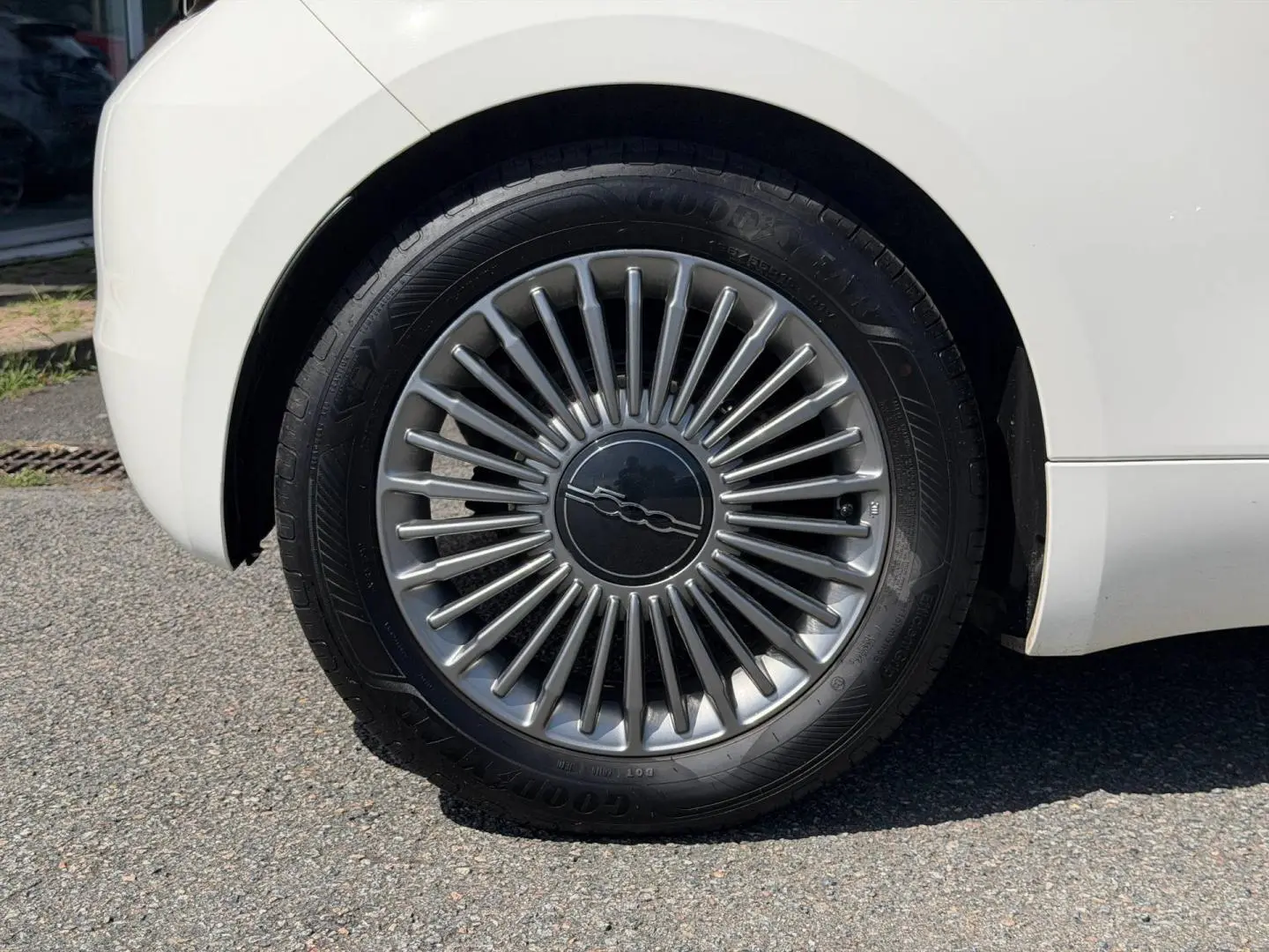 Gros plan sur la roue arrière droite blanche d'une Fiat 500 e 118ch MY23 avec jante argentée à rayons fins.
