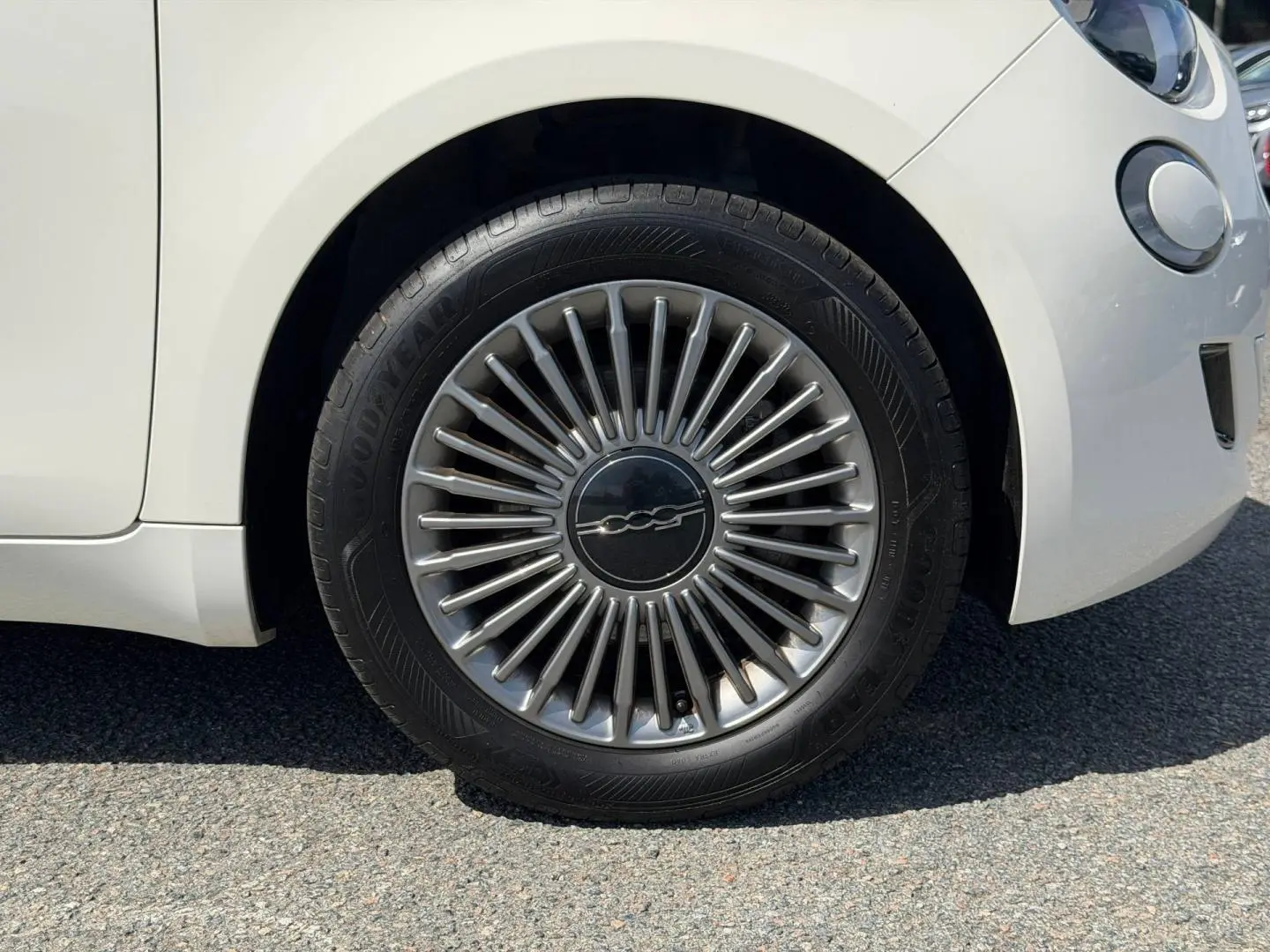 Gros plan sur la roue avant droite d'une Fiat 500 électrique blanche, avec jante argentée au design rayonné.