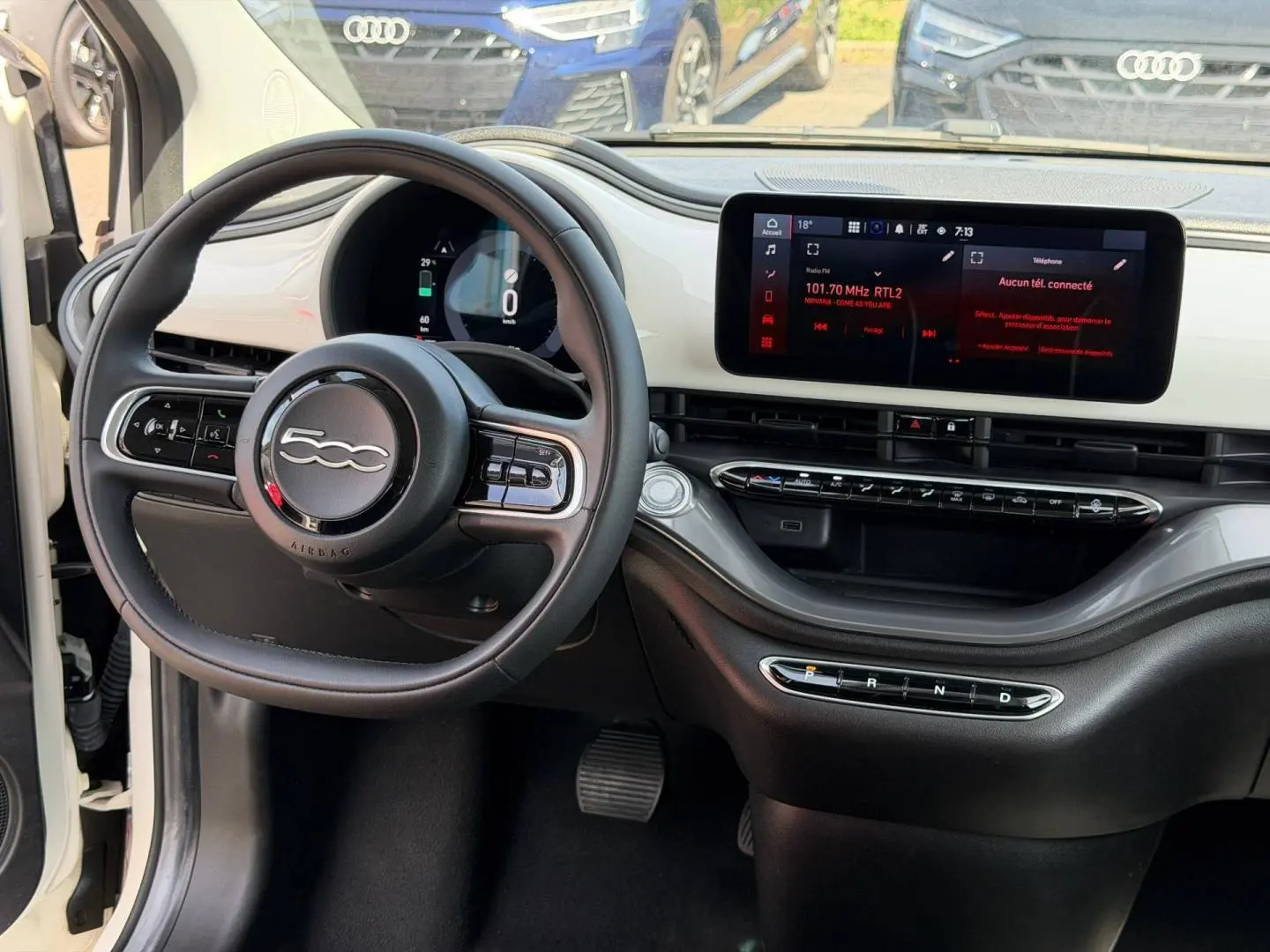 Vue intérieure du poste de conduite de la Fiat 500 e blanche 2023, avec volant multifonction et écran tactile central.
