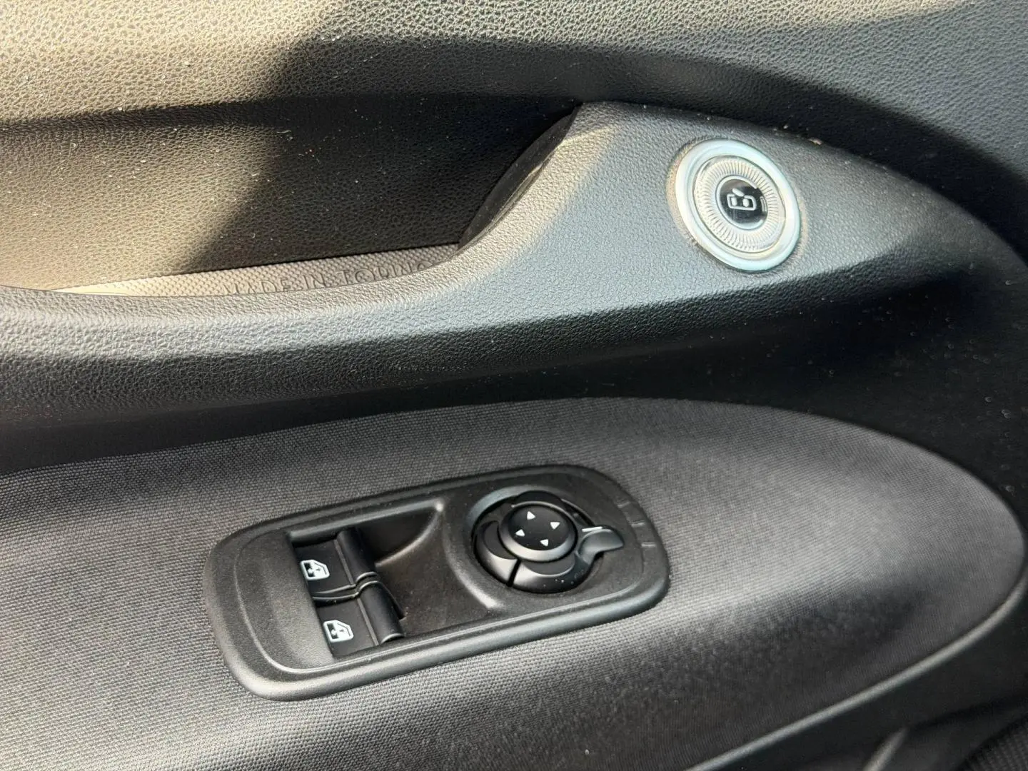 Gros plan sur la commande des vitres électriques et réglage des rétroviseurs côté conducteur de la Fiat 500 e blanche 2023.