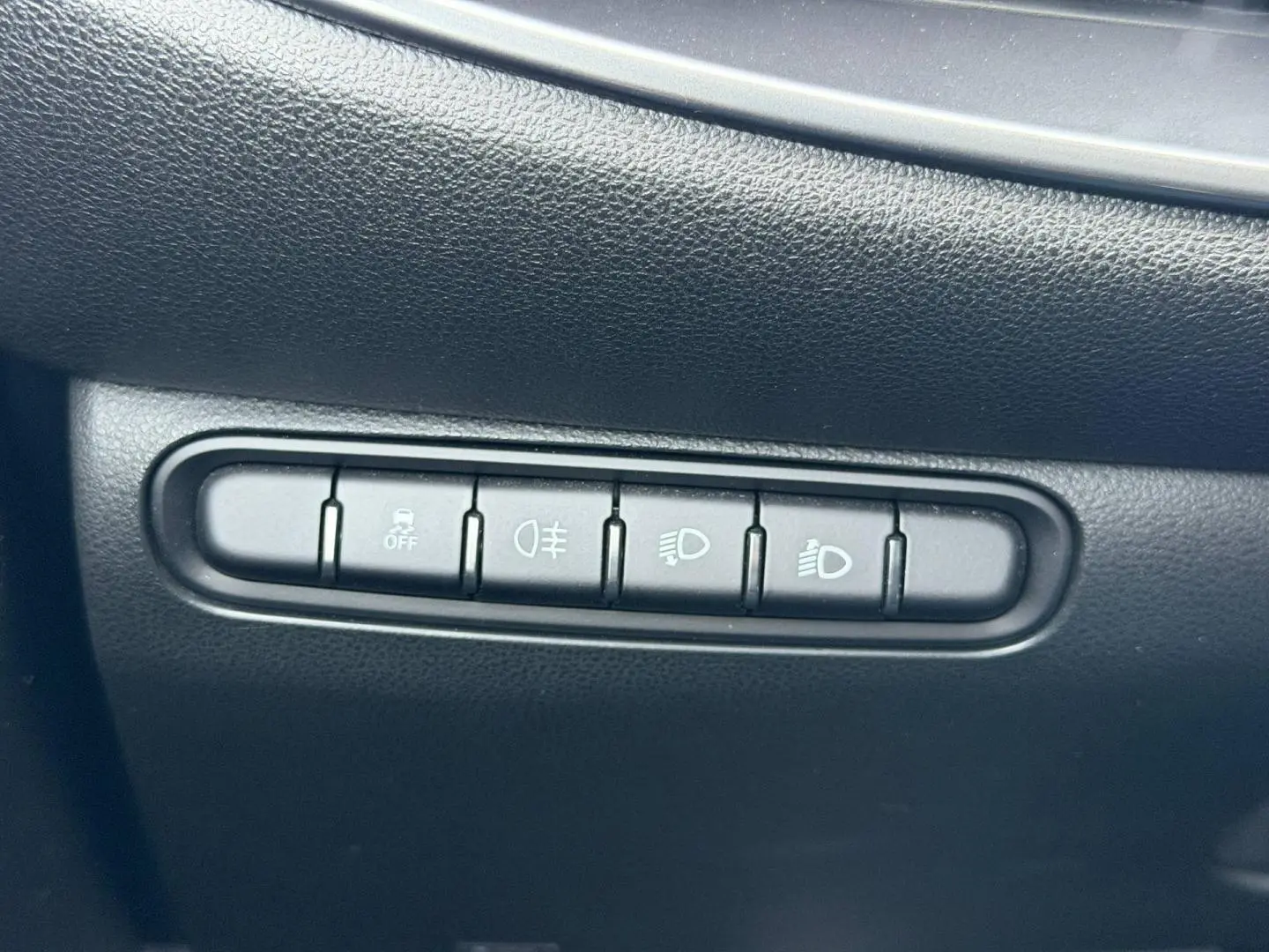 Gros plan sur les boutons de commande d'éclairage et d'assistance sur la planche de bord noire d'une Fiat 500 électrique blanche.