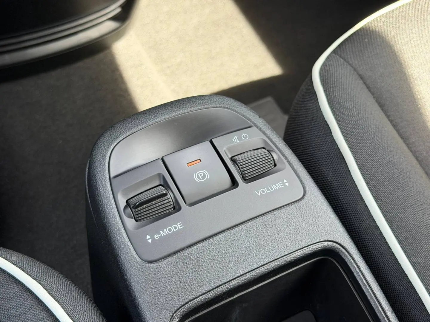 Gros plan sur la console centrale de la Fiat 500 électrique blanche 2023, avec commandes e-Mode et volume entre les sièges noirs.