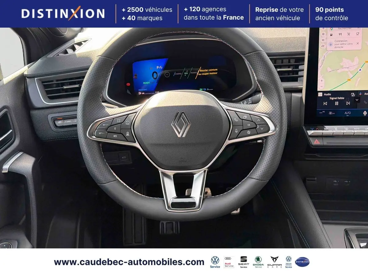Vue rapprochée du volant noir perforé avec logo Renault et tableau de bord numérique lumineux du Symbioz E-Tech.