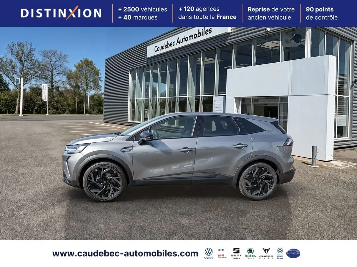 Profil droit de la Renault Symbioz E-Tech 160 ch gris métallisé, avec jantes alliage noires, devant un showroom.