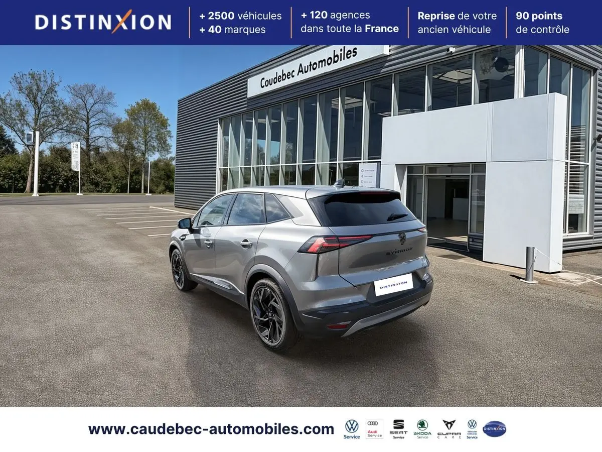 Vue 3/4 arrière droite d'un Renault Symbioz gris métallisé avec jantes noires devant un bâtiment moderne.
