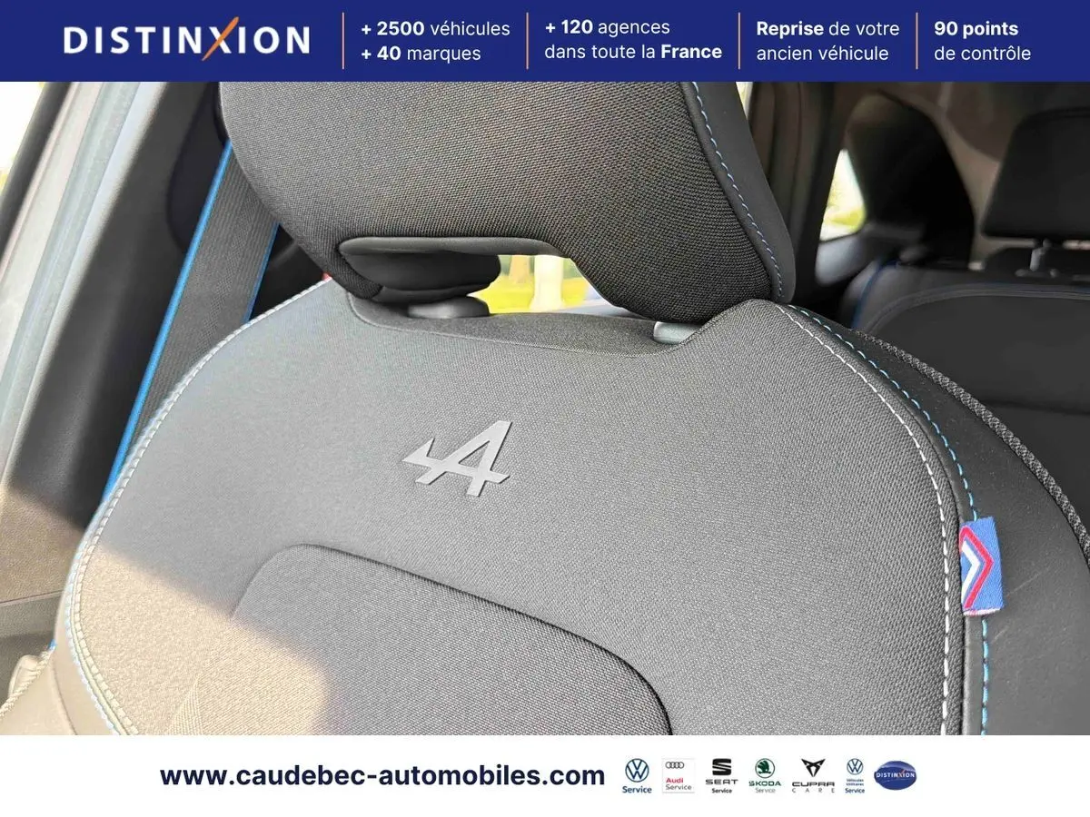 Gros plan sur l'appui-tête avant gris avec logo Alpine brodé et surpiqûres bleues dans l'habitacle du Renault Symbioz.