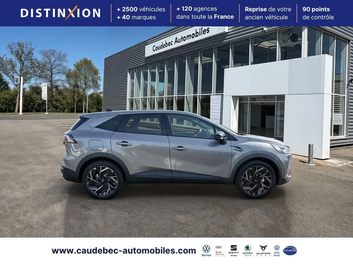 Vue de profil côté gauche d’un Renault Symbioz gris métallisé, avec jantes alliage 19 pouces, devant un bâtiment commercial.