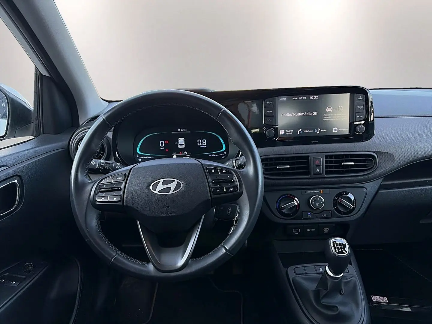 Vue intérieure du tableau de bord et volant cuir multifonction d'une Hyundai i10 blanche avec boîte manuelle et écran tactile.