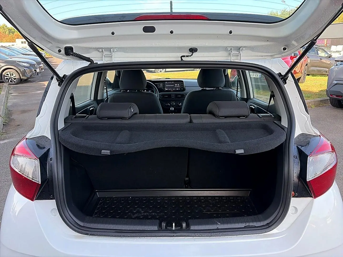 Vue arrière ouverte d'une Hyundai i10 blanche 2024, coffre vide avec tablette cache-bagages et intérieur noir visible.