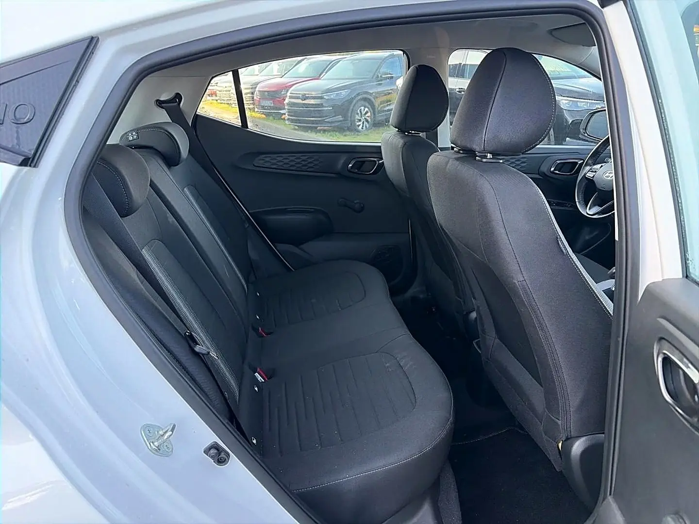Vue intérieure côté gauche montrant la banquette arrière noire et les sièges avant d'une Hyundai i10 blanche 2024.
