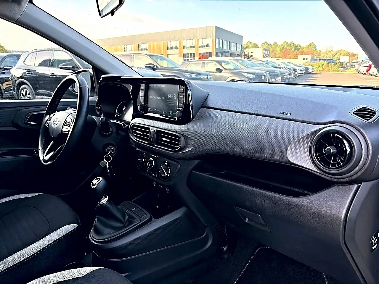 Intérieur avant droit de la Hyundai i10 blanche 2024, volant cuir, écran tactile et levier de vitesses manuel visible.