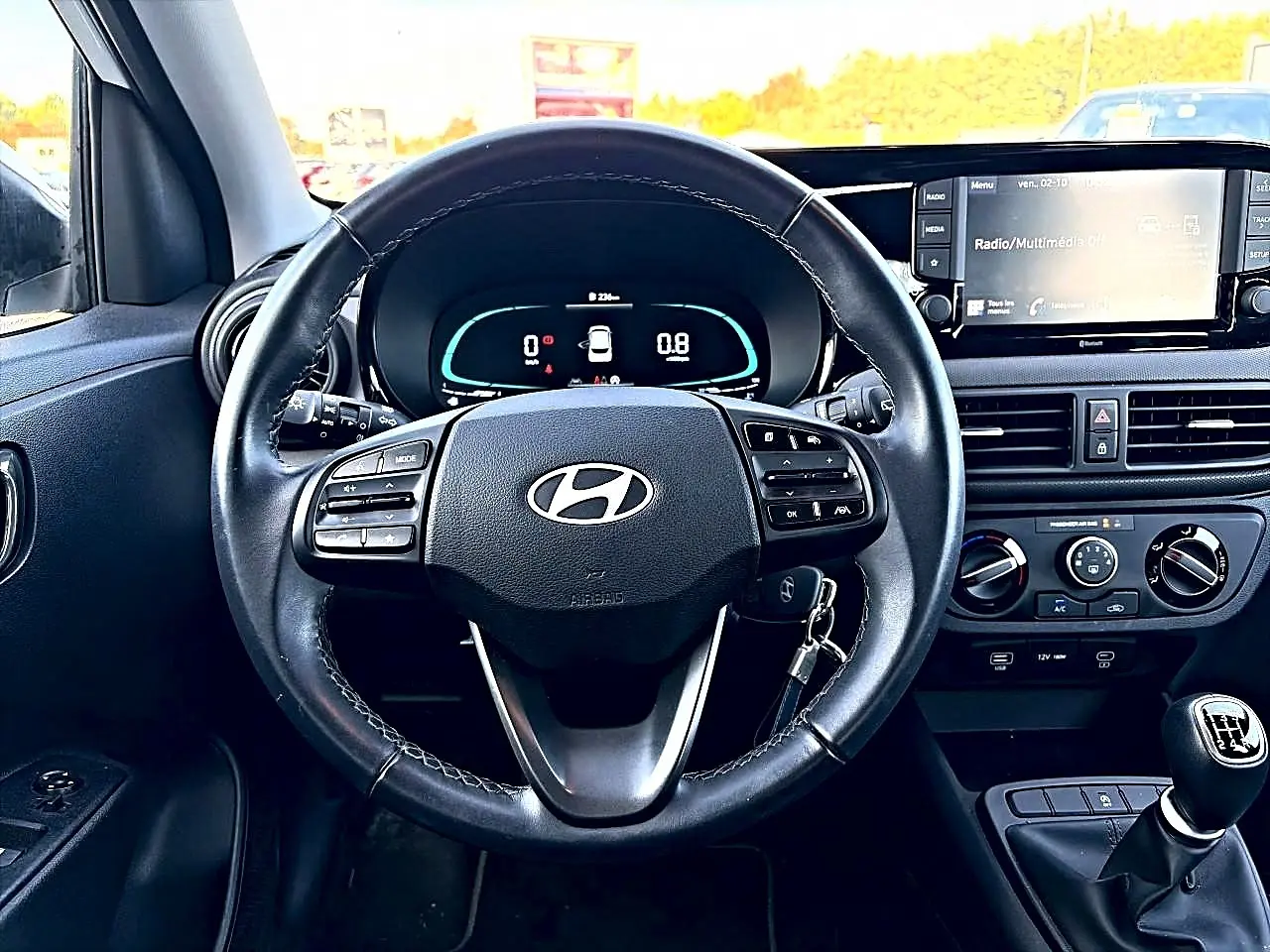 Vue intérieure centrée sur le volant cuir multifonction et le tableau de bord numérique d'une Hyundai i10 blanche 2024.