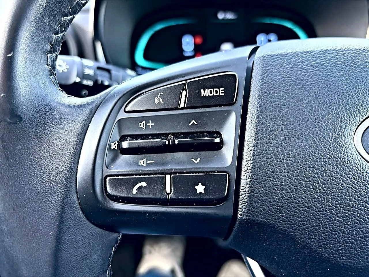 Gros plan sur les commandes audio et téléphoniques au volant cuir noir de la Hyundai i10 blanche 2024.