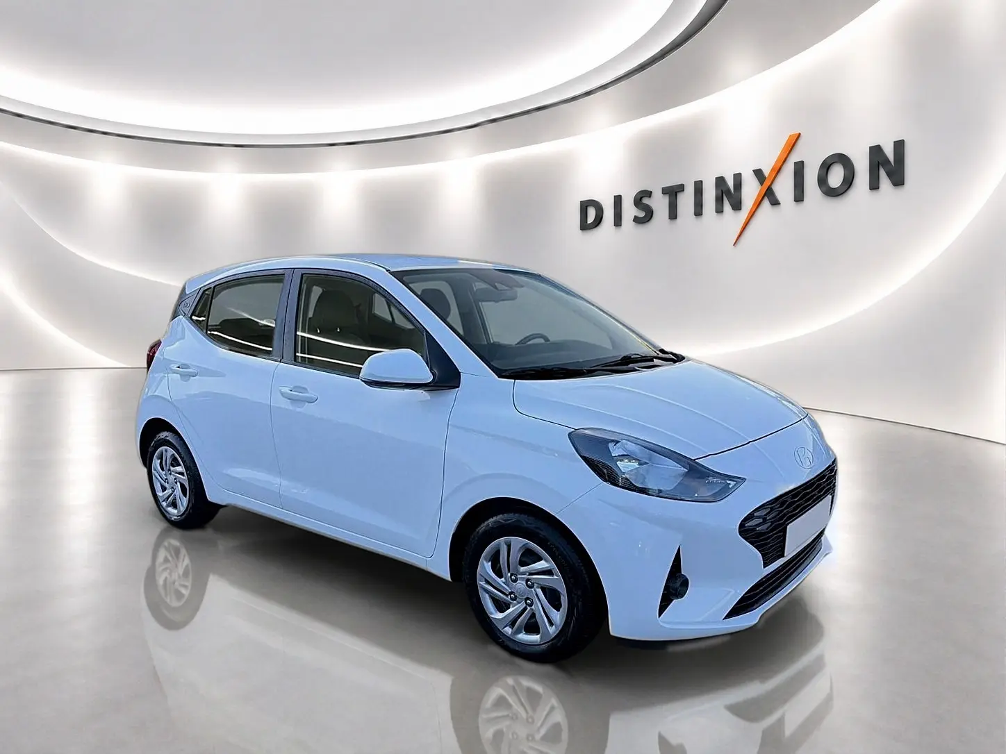 Hyundai i10 blanc vue 3/4 avant droit dans un showroom lumineux avec logo Distinxion en arrière-plan.