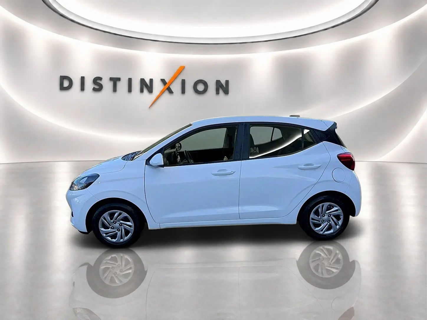 Profil droit de la Hyundai i10 blanche 2024, compacte et moderne, sur fond lumineux avec logo Distinxion en arrière-plan.