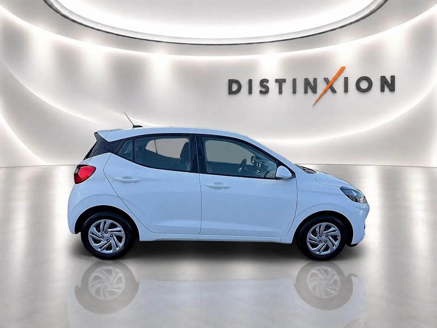 Profil droit d'une Hyundai i10 blanche 2024 dans un studio lumineux avec logo Distinxion en arrière-plan.