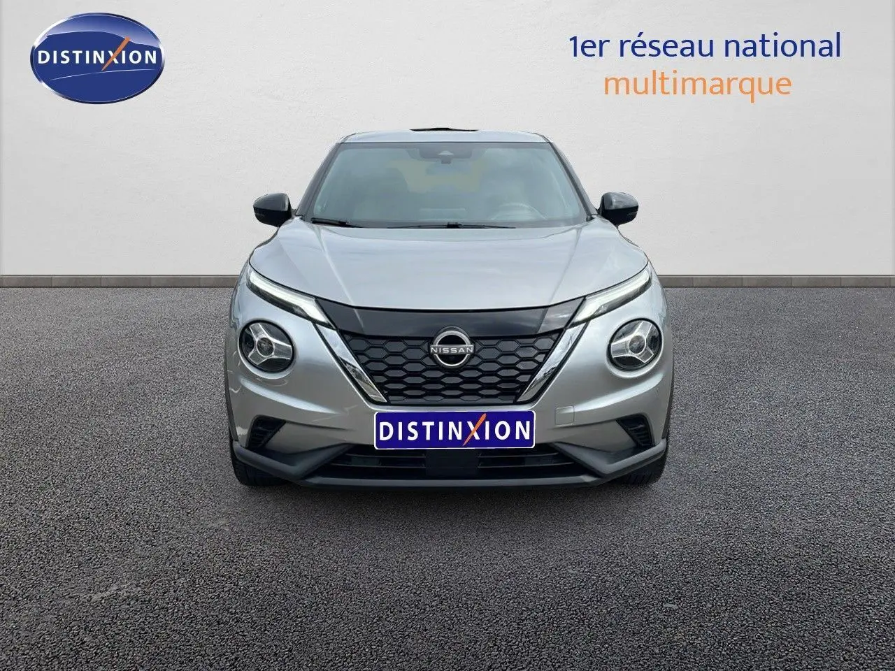 Vue frontale d'un Nissan Juke Hybrid gris perle métal avec calandre noire et phares ronds distinctifs.