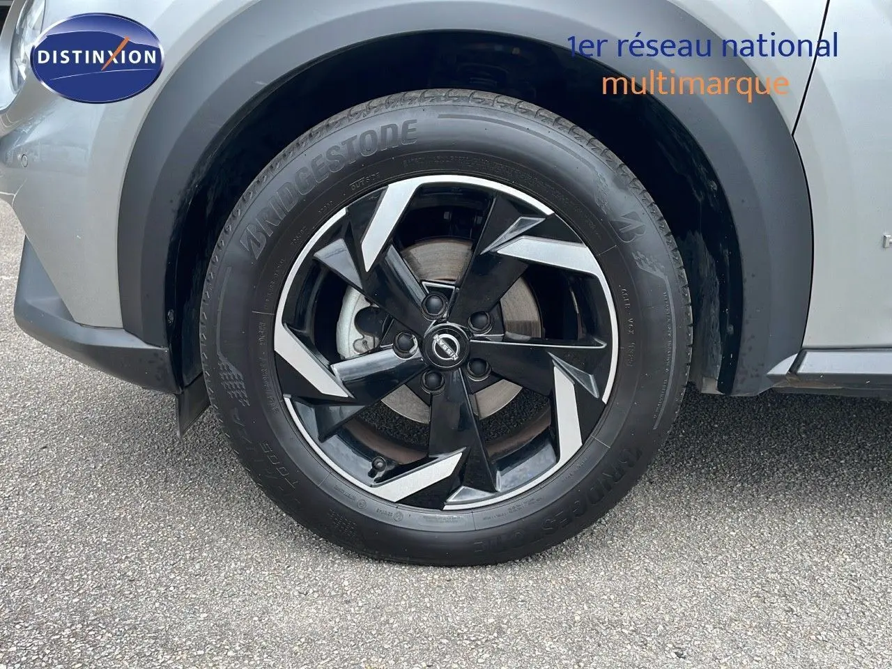 Gros plan sur la roue avant gauche du Nissan Juke Hybrid 143ch Business+ gris perle métal avec jante noire et argent.