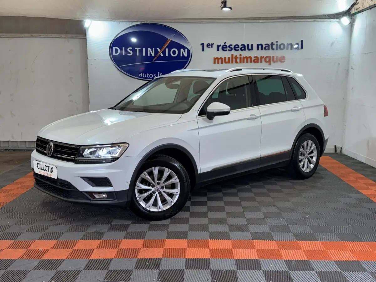 Volkswagen Tiguan blanc vu de 3/4 avant droit dans un showroom avec jantes alliage et barres de toit noires.