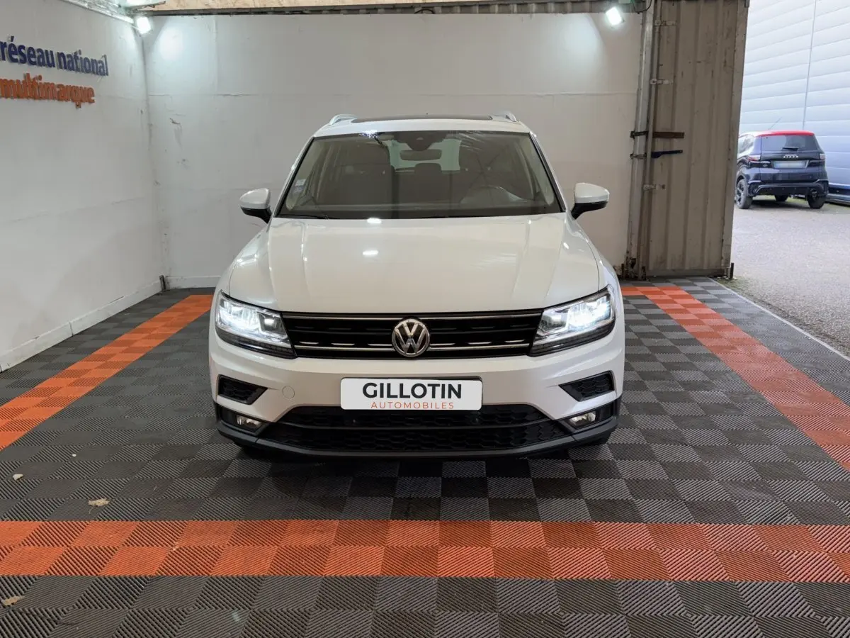 Volkswagen Tiguan blanc vue de face dans un showroom avec phares LED allumés et calandre noire.