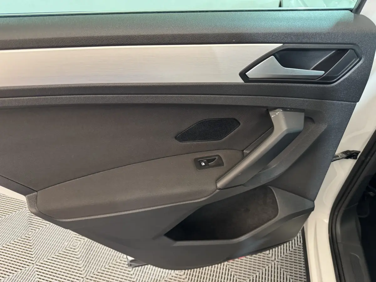 Intérieur côté gauche de la porte avant blanche du Volkswagen Tiguan 2020, avec garniture noire et poignée grise.