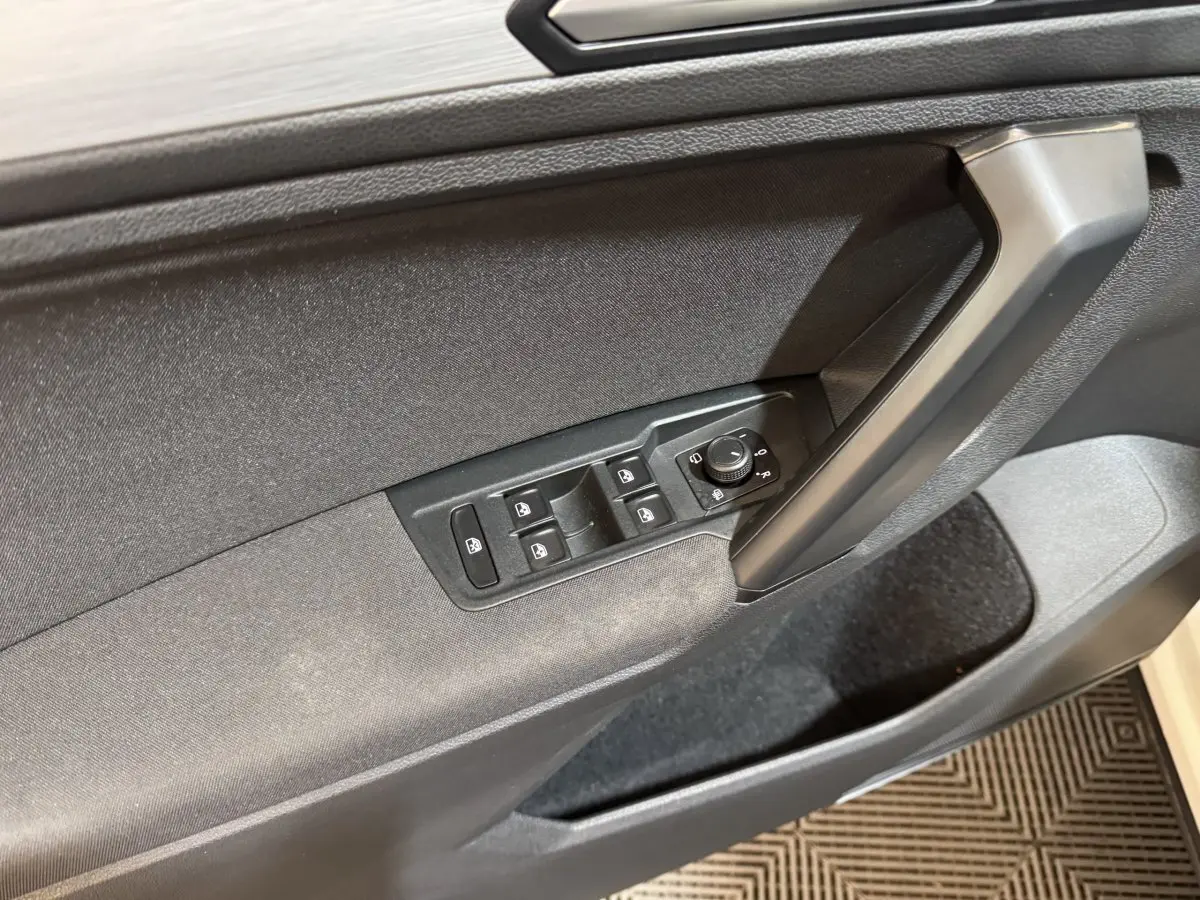 Gros plan sur la porte avant gauche du Volkswagen Tiguan blanc, montrant les commandes électriques des vitres et des rétroviseurs.