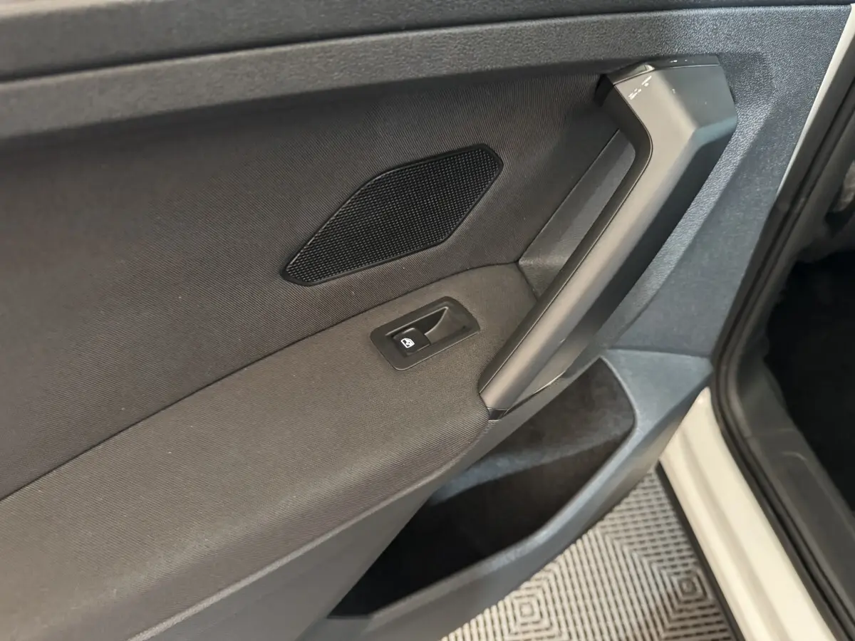 Gros plan sur la porte avant gauche noire du Volkswagen Tiguan blanc, avec poignée et bouton de vitre électrique.