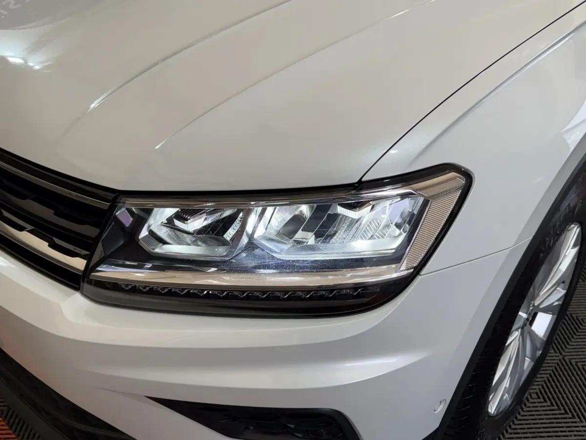 Gros plan sur le phare avant droit et la calandre du Volkswagen Tiguan blanc 2020, finition Confortline.