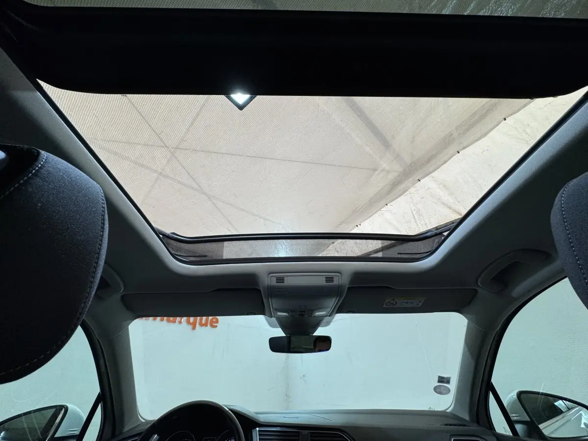 Vue intérieure du toit ouvrant panoramique du Volkswagen Tiguan blanc, avec tableau de bord et rétroviseur central visibles.