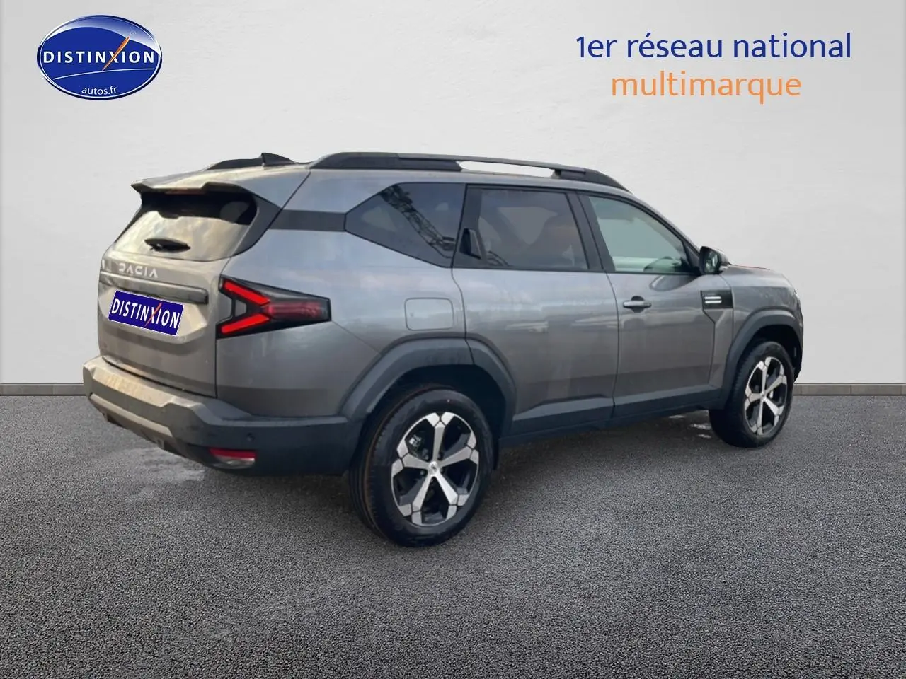 SUV Dacia Bigster gris schiste en 3/4 arrière droit avec jantes alliage diamantées et barres de toit visibles.