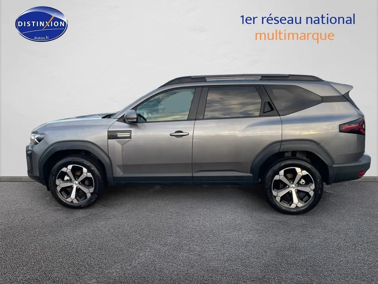 Vue de profil côté gauche du Dacia Bigster gris schiste avec jantes alliage diamantées et barres de toit noires.