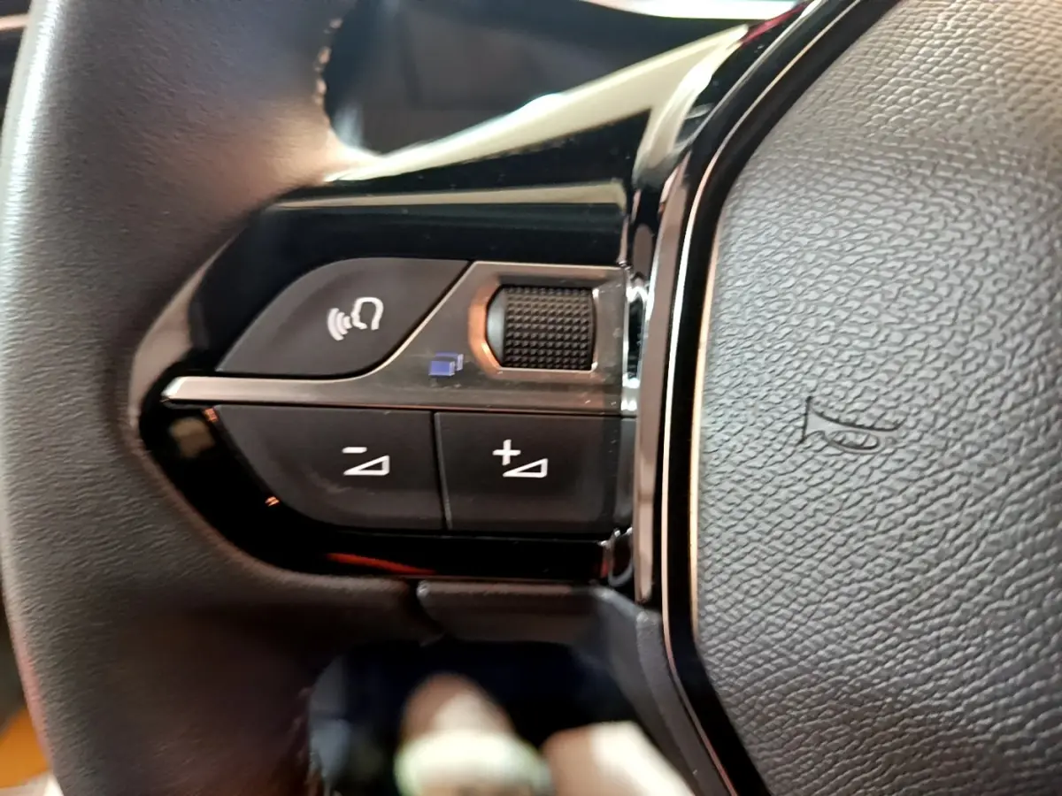 Gros plan sur les commandes multifonctions gauche du volant cuir de la Peugeot 208 jaune 2023.